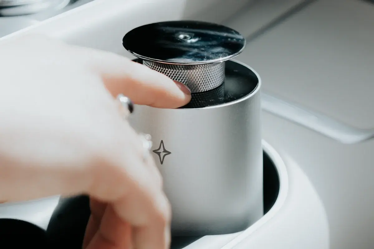 Close view of a hand holding Vessel 01 in a cup holder, showing its compact body and textured metal neck.