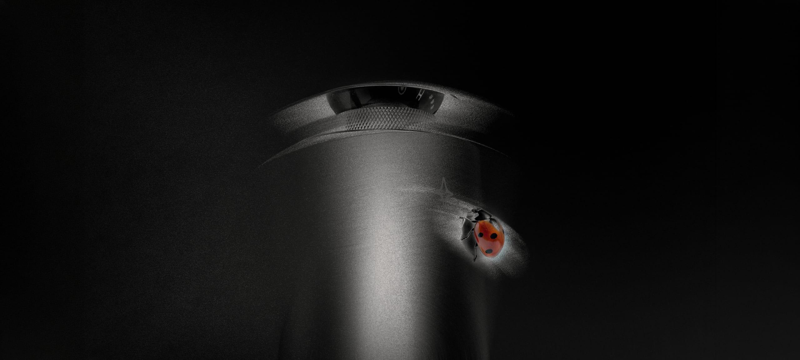 A Celestial Vessel diffuser lit from one side in the dark, with a ladybird resting on its brushed aluminium body.