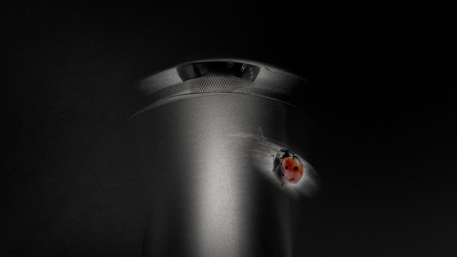 A Celestial Vessel diffuser lit from one side in the dark, with a ladybird resting on its brushed aluminium body.